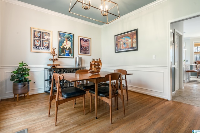 dining space with a wainscoted wall, light wood-style floors, ornamental molding, and a notable chandelier