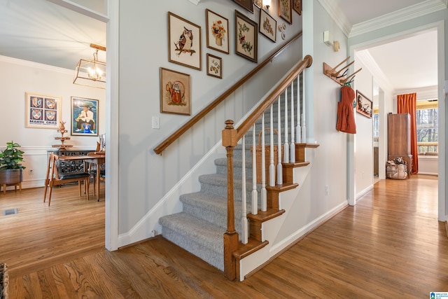 staircase featuring baseboards, a notable chandelier, wood finished floors, and crown molding