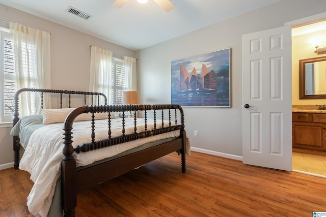 bedroom featuring a ceiling fan, baseboards, visible vents, ensuite bath, and light wood-type flooring