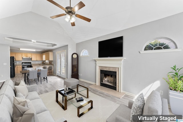 living area with a raised ceiling, a high end fireplace, light wood-style floors, baseboards, and ceiling fan