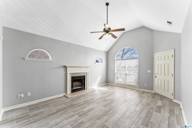 unfurnished living room with light wood-type flooring, visible vents, a fireplace with raised hearth, a ceiling fan, and baseboards