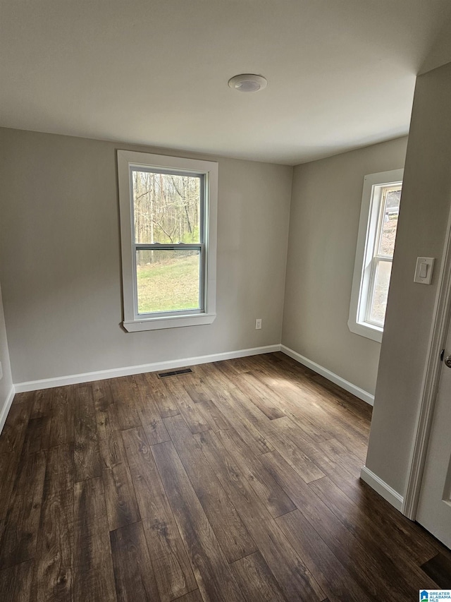 unfurnished room featuring dark wood-style floors, visible vents, and baseboards