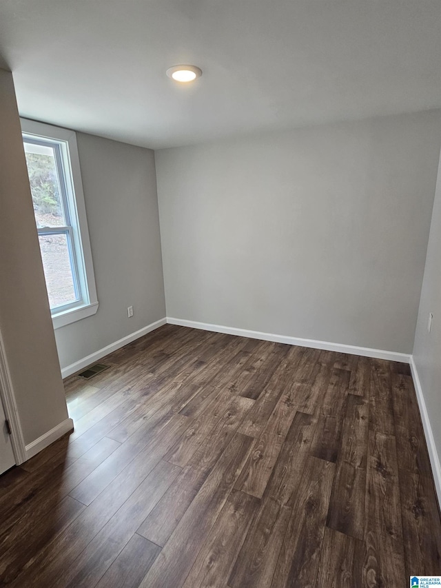 spare room featuring dark wood finished floors, visible vents, and baseboards