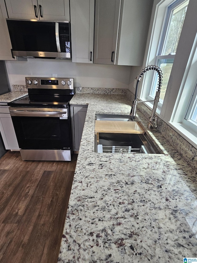 kitchen featuring light stone countertops, dark wood finished floors, gray cabinetry, a sink, and appliances with stainless steel finishes