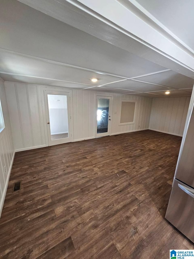 spare room with visible vents, beamed ceiling, dark wood-style flooring, and a decorative wall