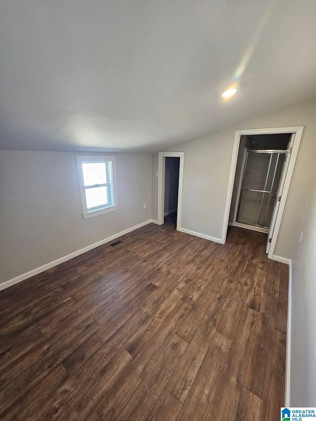 unfurnished bedroom featuring lofted ceiling, dark wood-style floors, baseboards, and visible vents