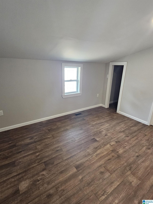 empty room featuring vaulted ceiling, baseboards, visible vents, and dark wood-style flooring