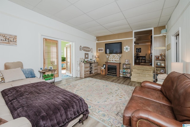 living area featuring a glass covered fireplace, wood finished floors, and a drop ceiling