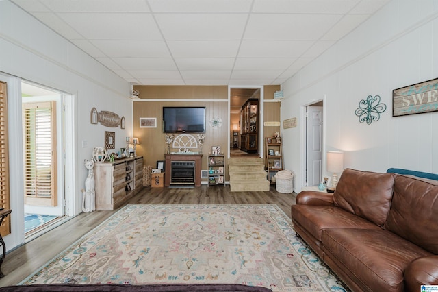 living room featuring a glass covered fireplace, a paneled ceiling, and wood finished floors