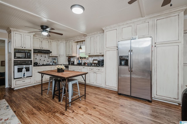 kitchen with dark countertops, oven, black microwave, under cabinet range hood, and stainless steel refrigerator with ice dispenser