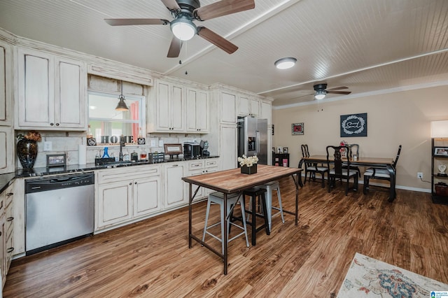 kitchen featuring wood finished floors, a sink, decorative backsplash, stainless steel appliances, and dark countertops