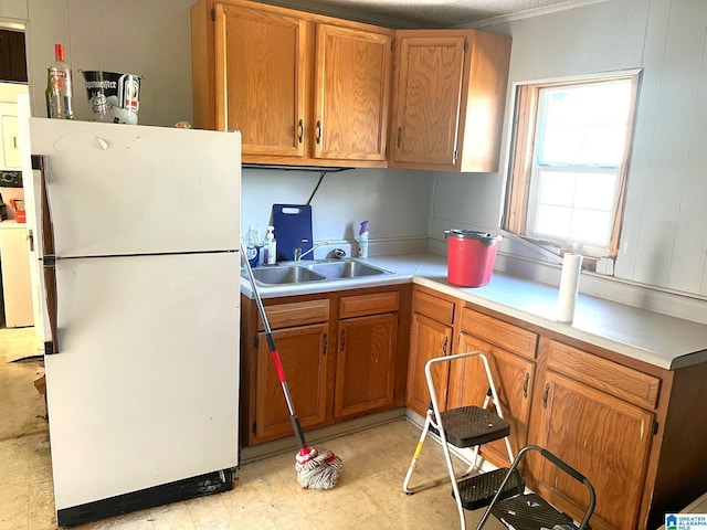 kitchen featuring brown cabinetry, light floors, freestanding refrigerator, a sink, and light countertops