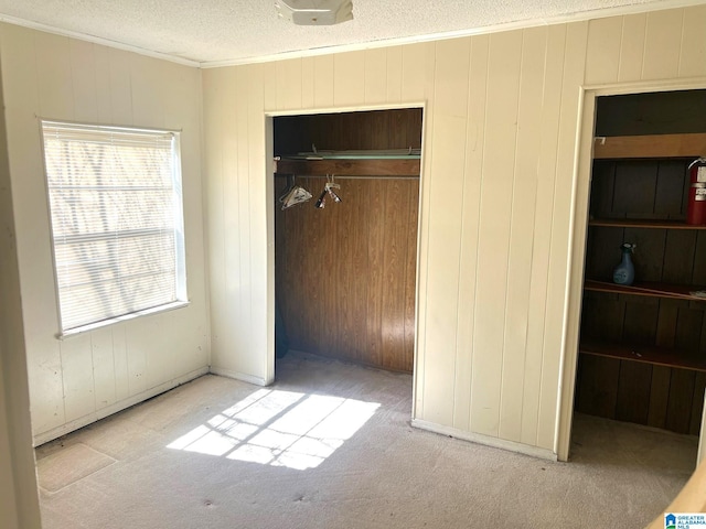 unfurnished bedroom with a textured ceiling, a closet, carpet, wood walls, and crown molding