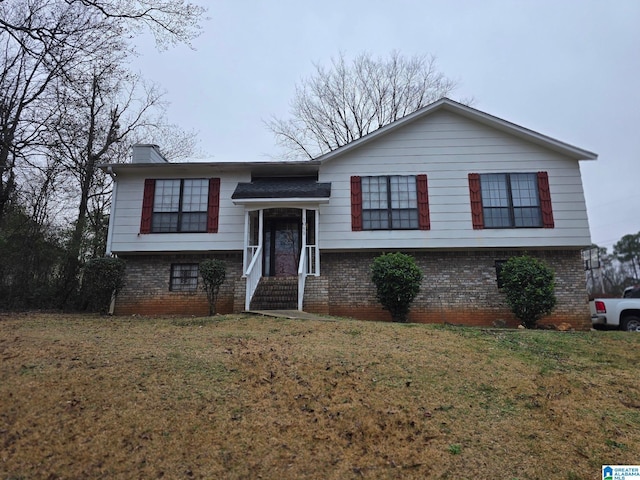 raised ranch with brick siding, a chimney, and a front lawn