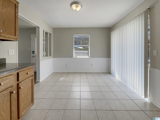 unfurnished dining area with light tile patterned floors and a wainscoted wall