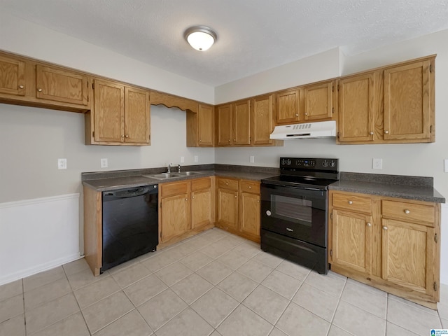 kitchen with black appliances, under cabinet range hood, a sink, dark countertops, and brown cabinetry