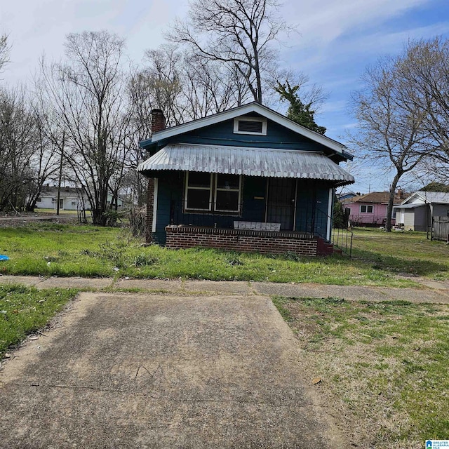 bungalow-style house featuring a chimney, covered porch, and a front yard