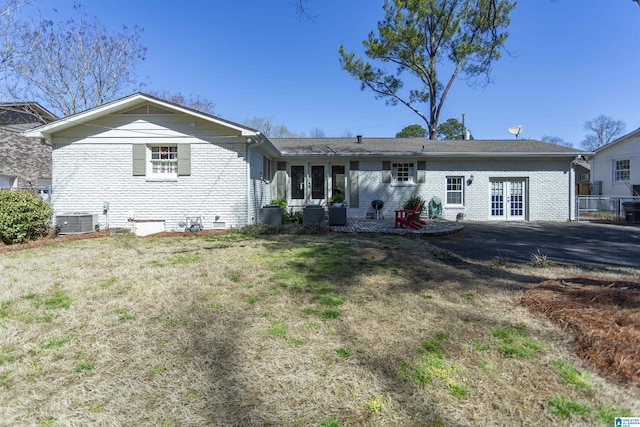 rear view of house featuring french doors, brick siding, central AC unit, and a lawn