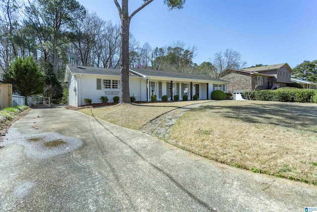 ranch-style house featuring brick siding, an attached garage, a front lawn, fence, and driveway