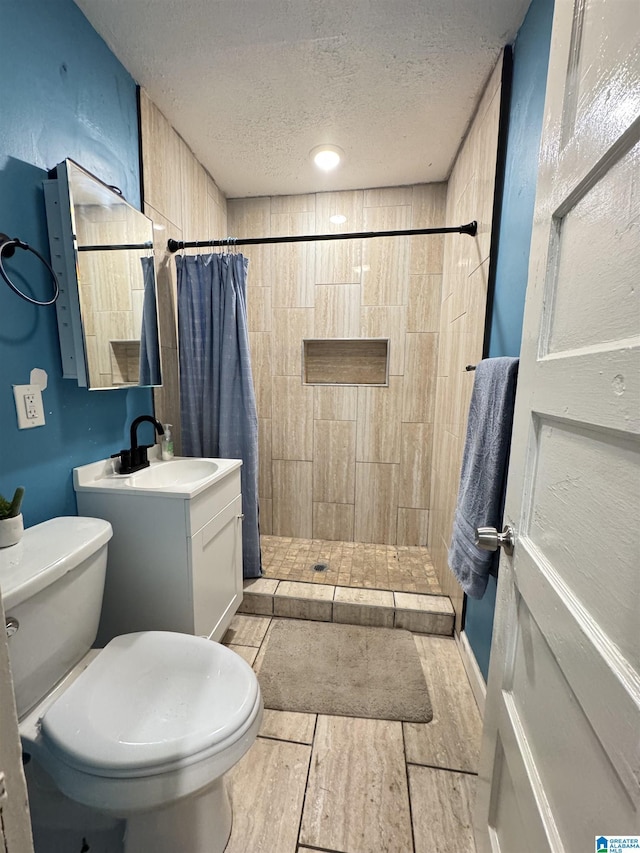 bathroom with wood finish floors, toilet, vanity, tiled shower, and a textured ceiling