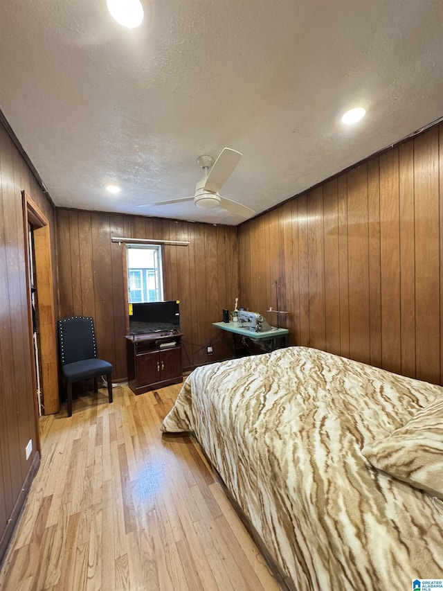 bedroom featuring ceiling fan, light wood-style floors, wood walls, and a textured ceiling