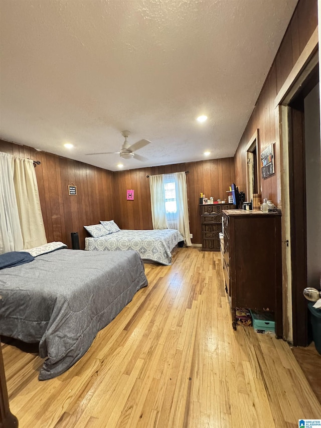 bedroom with light wood-style flooring, a ceiling fan, wood walls, and a textured ceiling