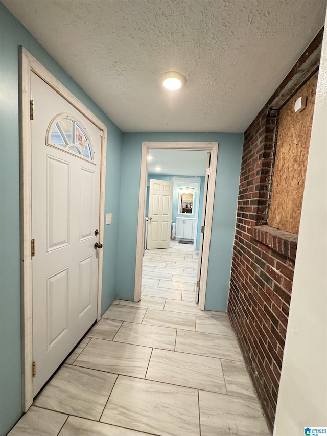 hallway featuring brick wall and a textured ceiling