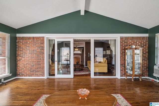 interior space with lofted ceiling with beams, wood finished floors, and brick wall