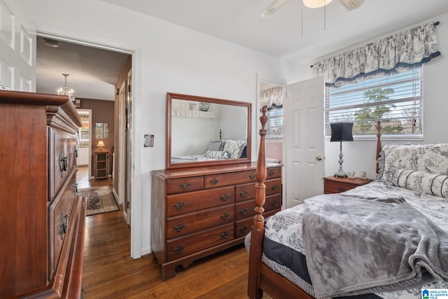 bedroom featuring ceiling fan with notable chandelier and dark wood-style floors