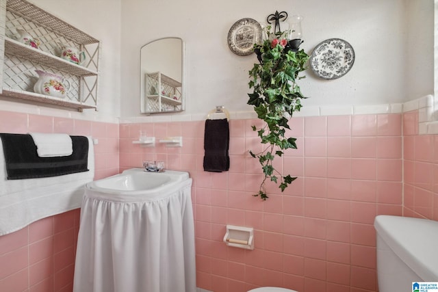 bathroom featuring a sink, tile walls, toilet, and wainscoting