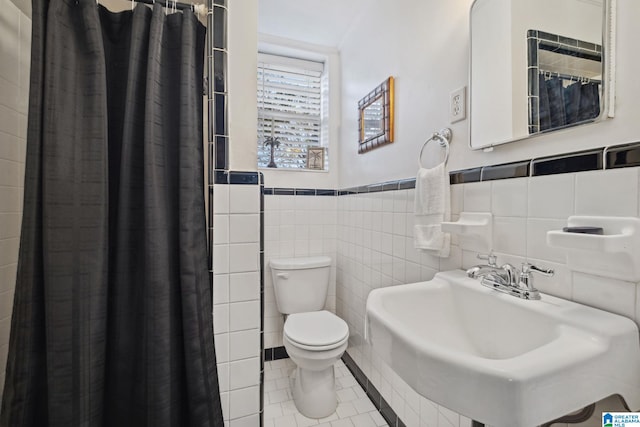 full bathroom featuring a wainscoted wall, toilet, a sink, tile walls, and tile patterned flooring