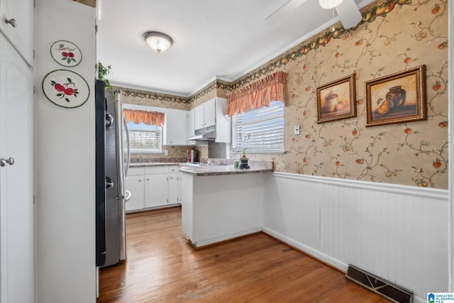 kitchen featuring visible vents, wallpapered walls, freestanding refrigerator, under cabinet range hood, and wainscoting