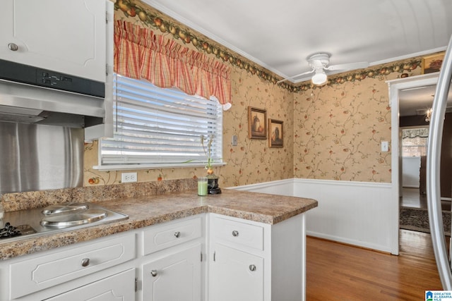 kitchen with a wainscoted wall, wood finished floors, white cabinetry, wallpapered walls, and ceiling fan