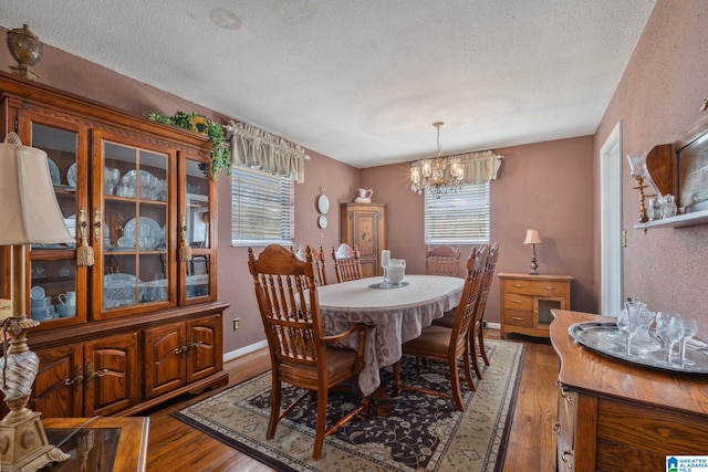 dining area with a notable chandelier, a textured ceiling, baseboards, and wood finished floors