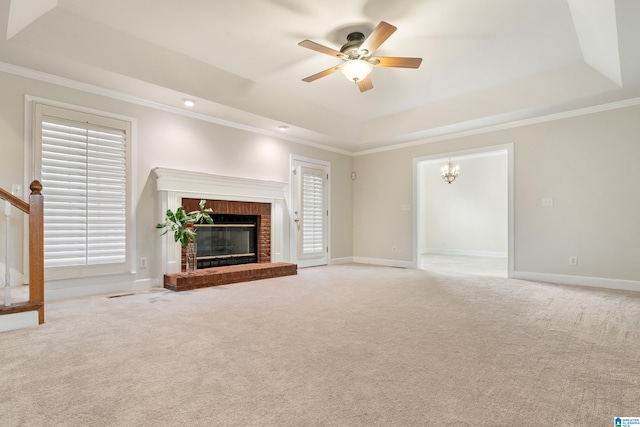 unfurnished living room featuring ceiling fan with notable chandelier, a tray ceiling, a fireplace, and light colored carpet