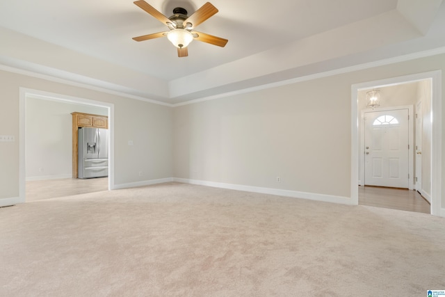 empty room featuring light colored carpet, a raised ceiling, baseboards, and ornamental molding