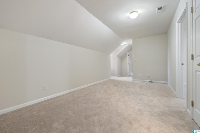 additional living space featuring visible vents, light colored carpet, baseboards, and vaulted ceiling