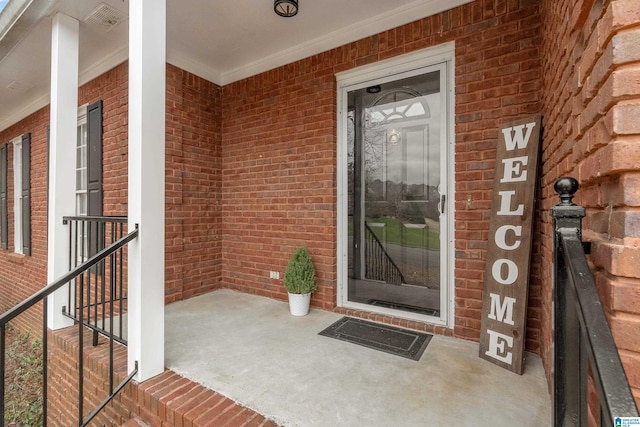 view of exterior entry featuring brick siding and covered porch