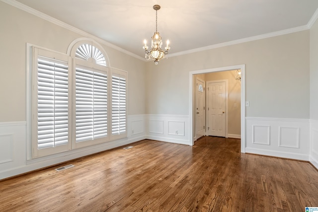 unfurnished dining area with visible vents, a wainscoted wall, a notable chandelier, wood finished floors, and crown molding