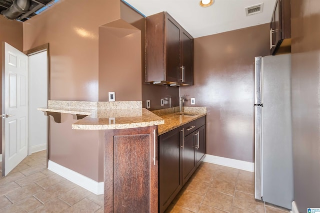 kitchen with light stone counters, visible vents, a peninsula, freestanding refrigerator, and a sink