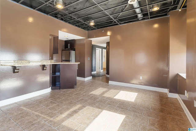 kitchen featuring light stone counters, baseboards, a peninsula, freestanding refrigerator, and a kitchen breakfast bar