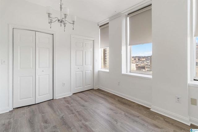 unfurnished bedroom featuring an inviting chandelier, baseboards, multiple closets, and wood finished floors