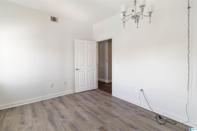 unfurnished room with a chandelier, visible vents, baseboards, and wood finished floors