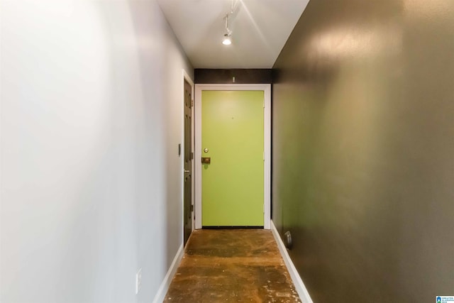 doorway to outside featuring track lighting, unfinished concrete flooring, and baseboards