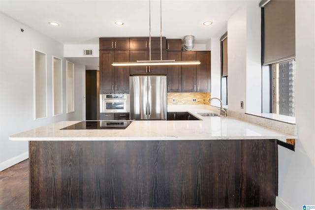 kitchen featuring visible vents, light stone counters, freestanding refrigerator, black electric cooktop, and a sink