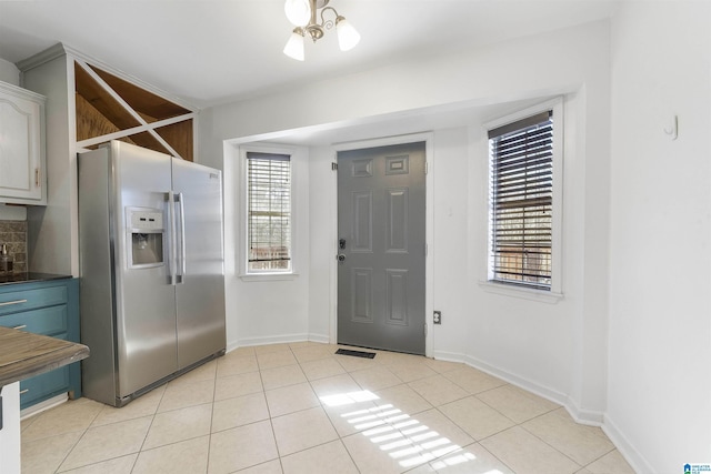 kitchen featuring light tile patterned floors, baseboards, dark countertops, and stainless steel refrigerator with ice dispenser