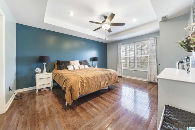 bedroom with hardwood / wood-style floors, visible vents, baseboards, a tray ceiling, and recessed lighting