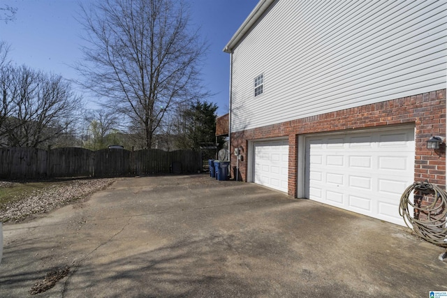 view of side of property featuring a garage, fence, brick siding, and driveway