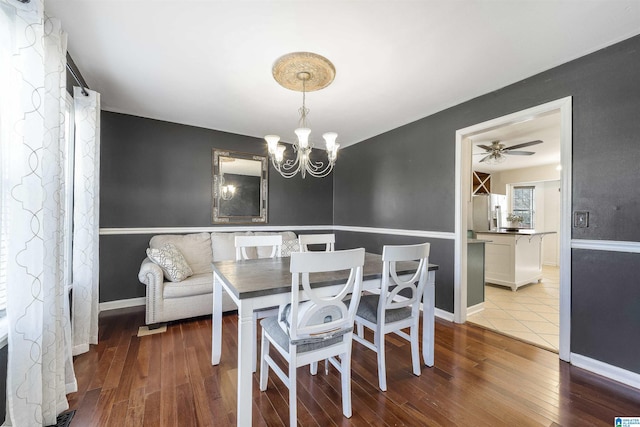 dining area featuring ceiling fan with notable chandelier, baseboards, and hardwood / wood-style floors