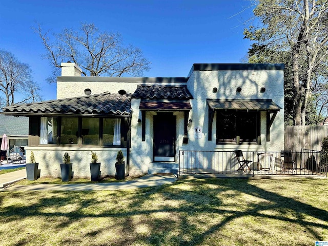 view of front of house with stucco siding, a chimney, a front lawn, and a tile roof